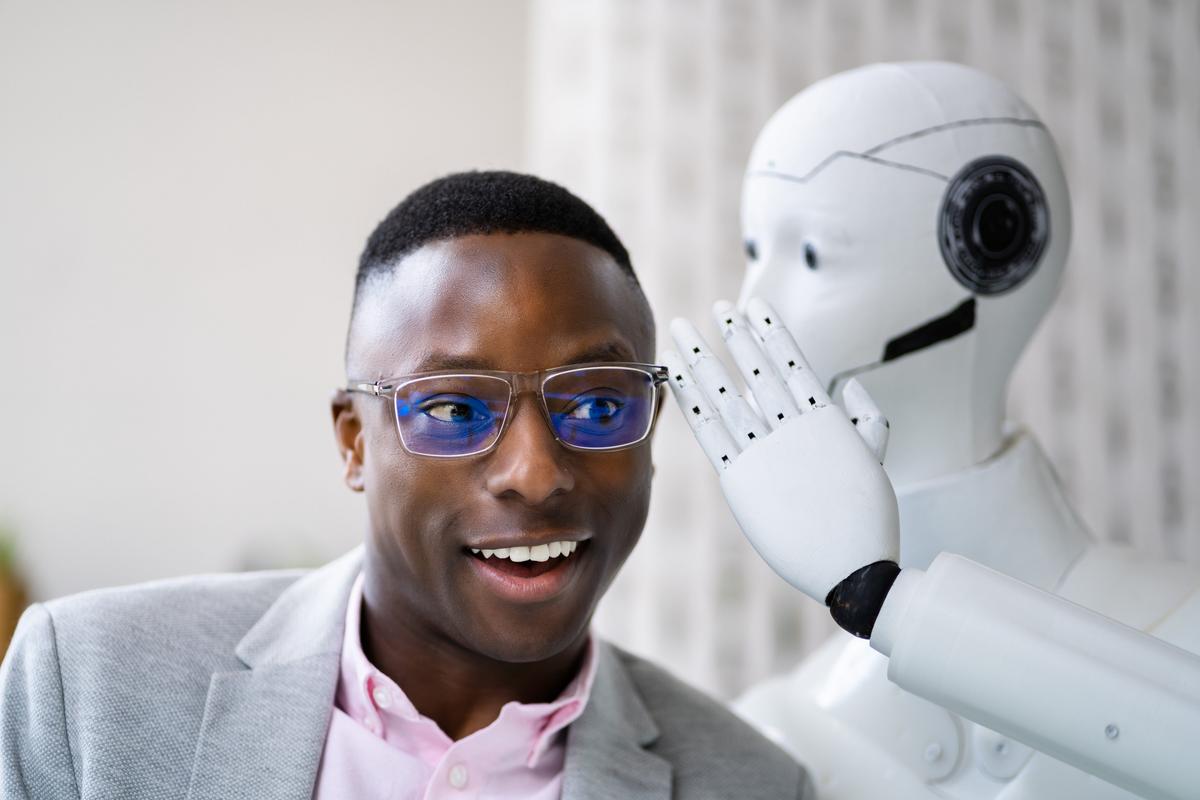 A smiling man sitting beside a humanoid robot.