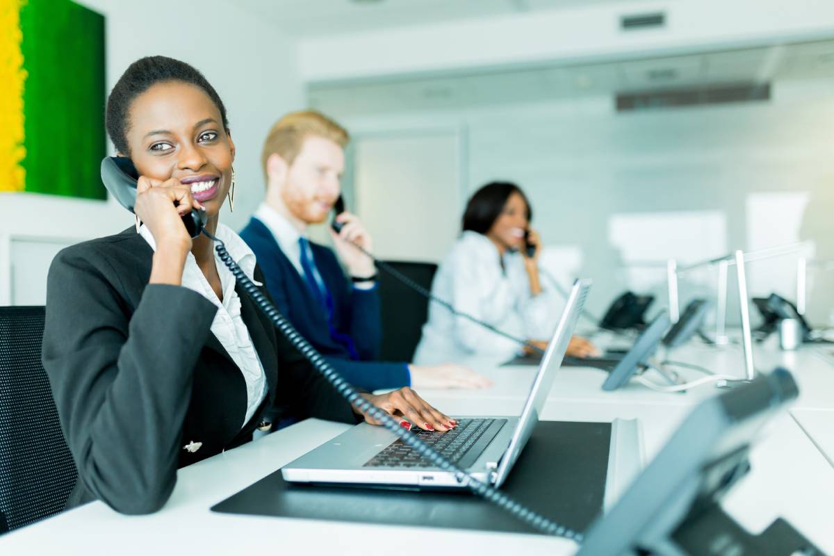 A woman using a laptop while talking on the phone, with her coworkers in the background