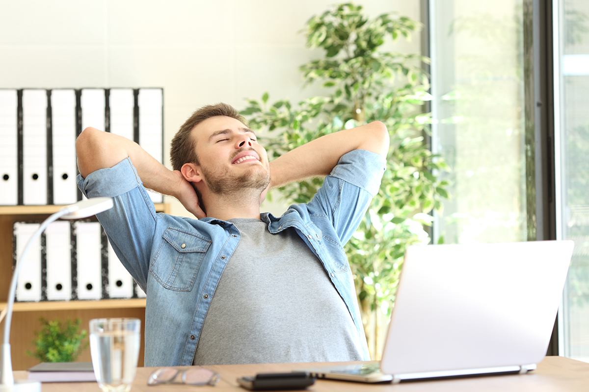 Happy businessman leaning back in chair with hands behind his head in home office setting.