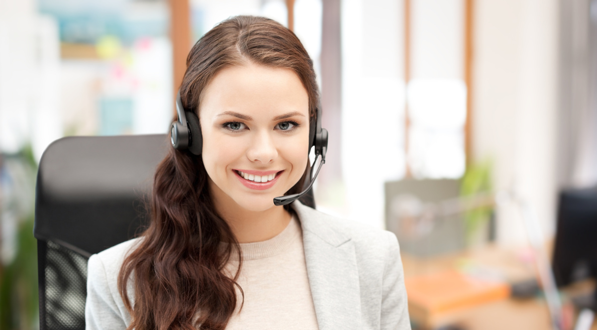 A smiling women sitting in an office chair wearing a headset, with her office out of focus in the background