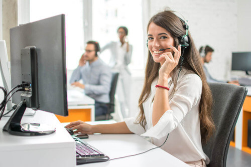 Smiling Customer Service Representative Wearing Headset Seated in Front of Desktop Computer